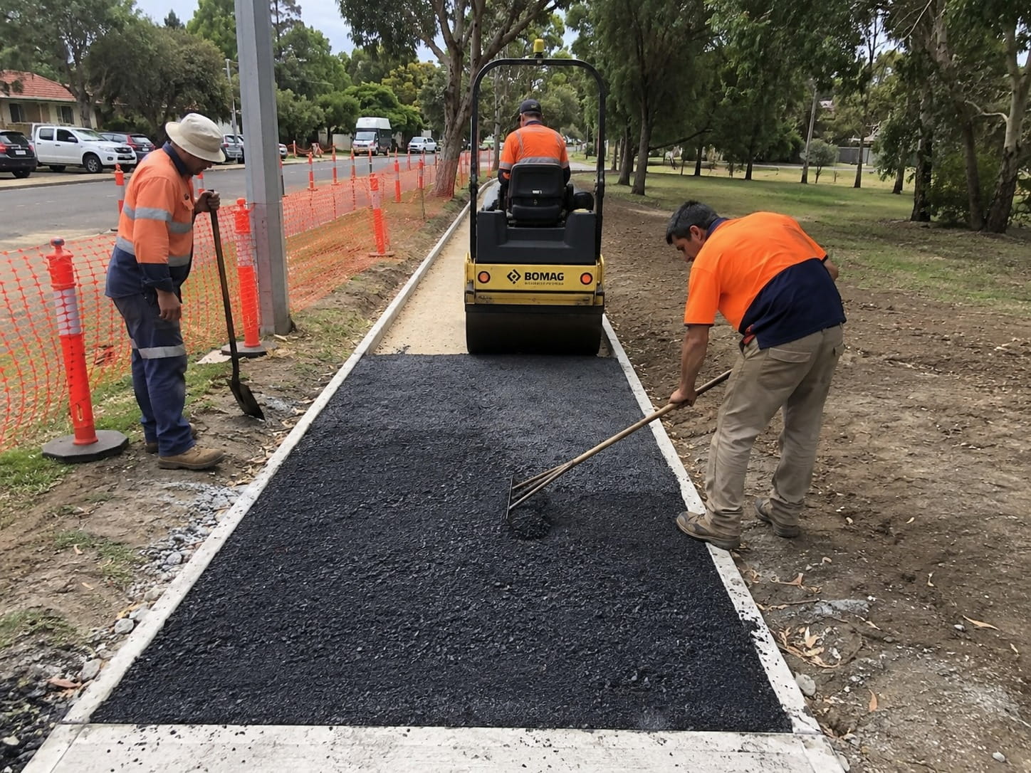 Civil paving crew compacting a new asphalt path beside a Perth street with a roller and safety fencing